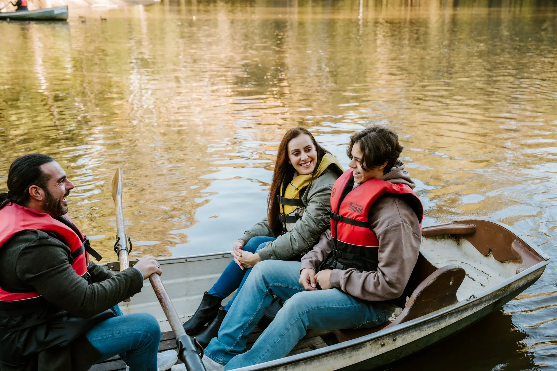 Three friends in life jackets laughing together in a rowing boat
