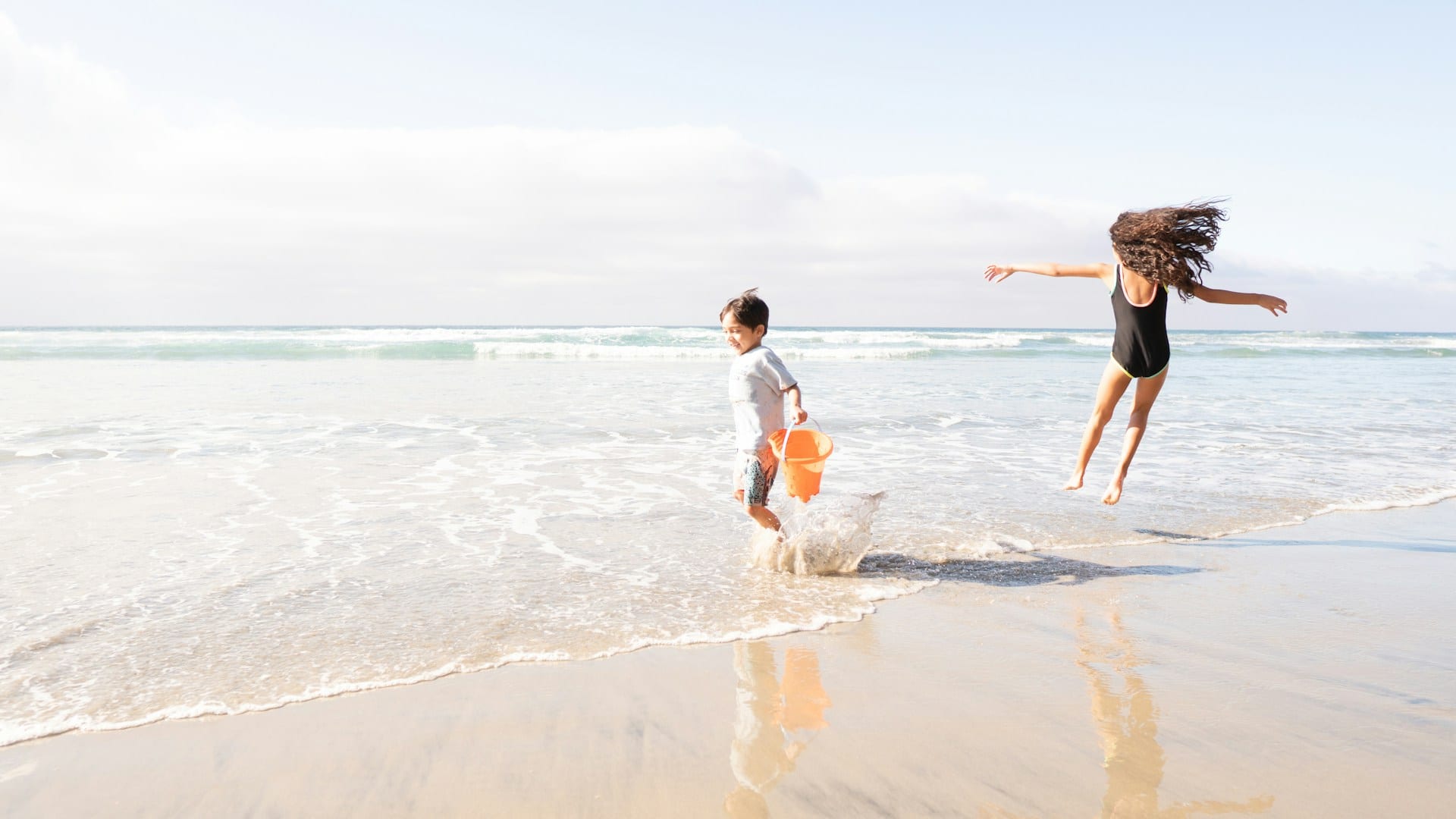 Two children running and splashing in the shallows at the beach